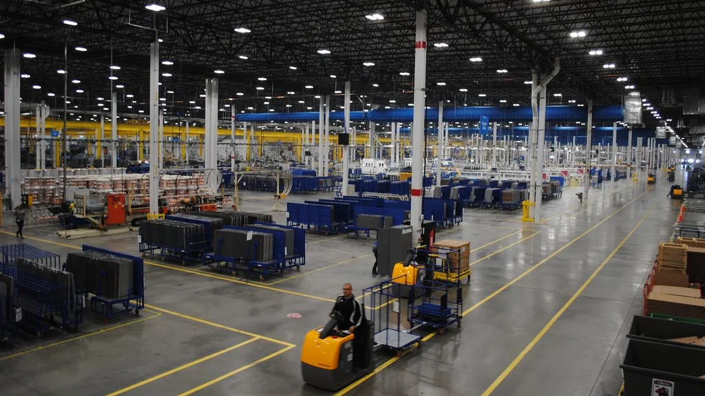 Wide view across a large manufacturing floor with rows of production equipment, workstations, and a person driving a material-handling vehicle in the foreground